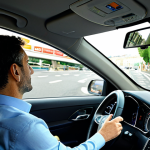 A professional traveler, fully clothed in a modest business casual outfit, sits thoughtfully in the driver's seat of a modern rental car, hands resting lightly on the steering wheel. A Crit'Air sticker is clearly visible on the car's windshield. The background shows a bustling urban scene in a French city, featuring complex road signage and a multi-lane roundabout, with other vehicles in the distance, conveying a sense of focused navigation. The image is captured with professional lighting, ensuring sharp details and correct proportions, showcasing a natural pose with well-formed hands and proper finger count. This is a safe for work, appropriate content, family-friendly image.
